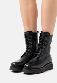Czarne skórzane botki za kostkę z okrągłym noskiem, sznurowanym przodem, wyścielanym kołnierzem oraz grubą, teksturowaną podeszwą. Posiadają zamek błyskawiczny po boku, co ułatwia zakładanie.