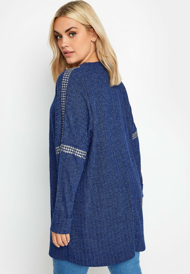 Langer blauer Cardigan aus strukturiertem Strick, mit silbernen Nietenakzenten an den Schultern und seitlichen Schlitztaschen.