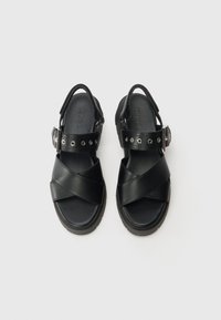 Black sandals with a cross-strap design, made of smooth leather. Features adjustable ankle strap with metallic accents and textured sole.