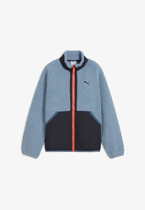 Világoskék bolyhos dzseki fekete alsó résszel, narancssárga cipzárral és tengerészkék részletekkel. Magas gallérral és textúrált felülettel rendelkezik.