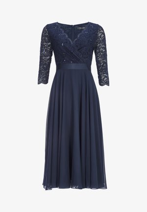 Abito blu navy con corpo in pizzo, maniche a tre quarti, design intricato di paillettes, fascia in satin in vita e gonna fluente. Chiusura con zip sul retro.