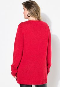 Czerwony sweter z dzianiny o luźnym kroju, długich rękawach i ściągaczu na dole. Miła w dotyku tekstura z lekko oversize'owym wzorem.