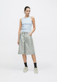 Ανοιχτό μπλε ριμπ αμάνικο τοπ με μικρό λογότυπο, σε συνδυασμό με γυαλιστερά ασημί σορτς με φαρδιά πόδια και ανοιχτό γκρι αθλητικά παπούτσια. Ορατές μαύρες κάλτσες.