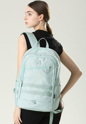 Zaino di un leggero verde menta realizzato in tessuto testurizzato, con una tasca frontale con zip, tasche laterali in rete e spallacci regolabili.