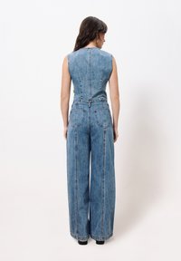 Denim-Overall mit ärmellosem Design, hellblauer Farbe, weitem Bein, auffälligen Nähten und Gesäßtaschen, mit tailliertem Schnitt.