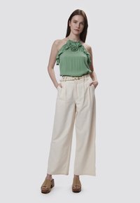 Top verde a halter con scollatura arricciata, abbinato a pantaloni a gamba larga beige a vita alta e sandali con piattaforma marroni.