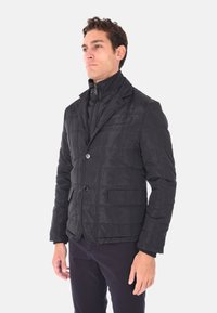 Giacca nera trapuntata con colletto alto, due bottoni e tasche frontali; presenta una texture liscia e lucida e un design strutturato.