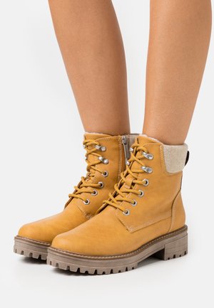 Bruna läderankelboots med fleecekrage, rund tå och robust strukturerad sula. Utrustad med metalldetaljer och snörning framtill.