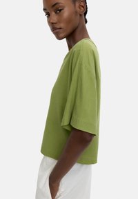 Zielona koszulka z krótkim rękawem o luźnym kroju i okrągłym dekolcie, charakteryzująca się gładką fakturą i starannym przeszyciem.