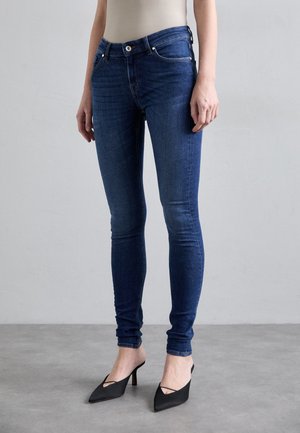 Niebieskie skinny jeansy o gładkiej teksturze denimu, wysoki stan i pięć kieszeni, zestawione z czarnymi szpilkami o szpiczastym nosku.