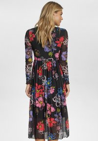 Långärmad, svart blommig klänning med färgglada blommönster. Har en figursydd bodice och en svävande kjol som faller nedanför knäna.
