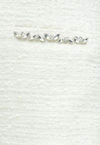 Biała tkanina o fakturze z dekoracyjnym rzędem pięciu przezroczystych kamieni szlachetnych o różnych kształtach i rozmiarach, podkreślająca górną część.