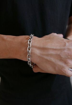 Silver chain bracelet on a wrist, featuring interconnected oval links with a smooth, polished finish against a dark shirt background.