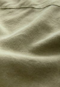 Béžová tkanina s textúrovaným povrchom, zobrazujúca jemné záhyby a vrásky. Materiál pôsobí ľahko a je tkaný, čo zvýrazňuje jemné detaily.