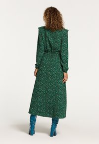 Grön blommig maxiklänning med långa ärmar, volangdetalj på axlarna och ett bälte i midjan. Matchas med knähöga blå stövlar.