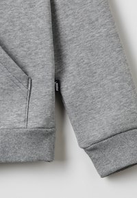 Grå sweatshirt med ett mjukt, texturerat tyg, ribbade ärmmuddar och en lomme framtill. En liten tygmärkning syns på sidsömmen.