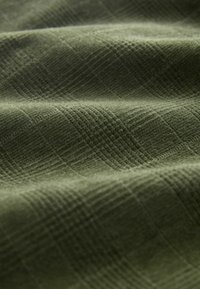 Material texturat de culoare verde măsliniu, cu un model în rețea, având o textură țesută și linii contrastante, creând o apariție moale, dar bine definită.