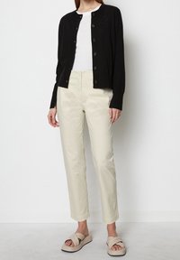 Czarny dziergany kardigan, biały t-shirt, beżowe spodnie 3/4 oraz beżowe sandały z grubymi paskami. Gładkie tekstury i prosty design.