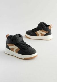 Baskets montantes noires avec des accents beiges, semelle en caoutchouc blanc, tige en textile et synthétique, dotées de lacets et d'une sangle à boucle.