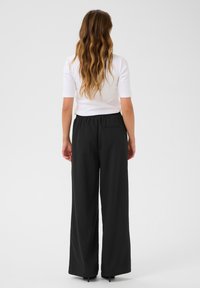Pantalons noirs à jambes larges avec un élastique à la taille et une seule poche arrière. Associés à un haut ajusté à manches courtes blanc. Tissu au toucher lisse.