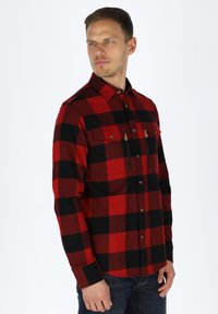 Rood en zwart flanellen shirt met een geruit patroon, lange mouwen, twee borstzakken en knoopsluiting aan de voorkant, gemaakt van zachte stof.