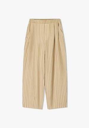 Beige pruhované kalhoty s elastickým pasem, dvěma bočními kapsami, volným střihem a vertikálními černými pruhy pro detail.