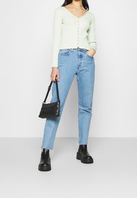 Ljusgrön ribbad kofta med knappstängning, högmidjade blå jeans och svart kviltad handväska; svarts chunky ankelstövlar med fransdetalj.