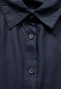 Camicia blu navy con colletto classico, dotata di chiusure a bottone e una texture liscia, realizzata in tessuto leggero.