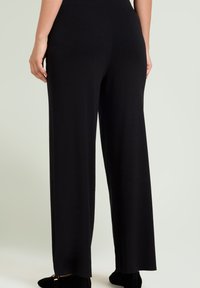 Zwarte wijde broek gemaakt van zachte stof met een gladde textuur. Bevat een hoge tailleband en heeft een rechte pasvorm die tot de enkels reikt.