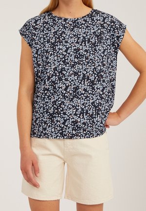 Granatowa koszula w kwiatowy wzór z rękawkami typu kaptur, ozdobiona jasnoniebieskimi i rdzawymi akcentami, noszona z kremowymi szortami, tworząc casualowy wygląd.