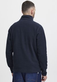 Sudadera de forro polar azul marino con cuello alto y mangas largas. Textura suave, dobladillo recto y detalles mínimos en la parte posterior.