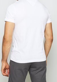 Camiseta blanca de manga corta con escote redondo, que presenta una textura de algodón suave y un diseño simple y limpio. La vista posterior no muestra impresiones.