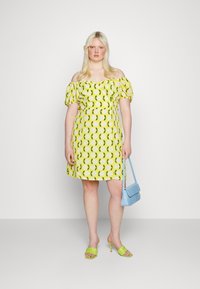 Vestido amarelo com flores, mangas bufantes, cintura ajustada e saia rodada. Combinado com sandálias de salto verdes e uma pequena bolsa azul.