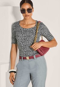 Leopardenmuster-Bluse, graue Tailored-Hosen, bordeauxfarbener Gürtel mit Logo, weiß-schwarze Armreifen und eine bordeauxfarbene, gesteppten Handtasche mit Kettenriemen.