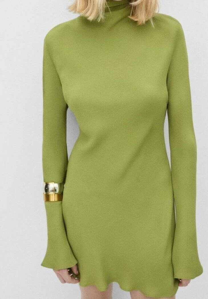Femme portant une robe moulante à manches longues de couleur vert citron avec un col montant et des poignets évasés, accessoirisée avec deux bracelets métalliques.