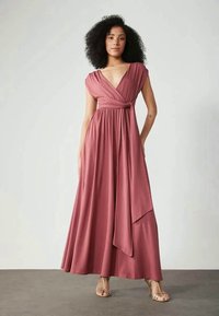Vestido longo e fluido em tecido rosa desbotado. Apresenta um corpete envolto, mangas curtas tipo capa e uma cintura atada. Textura suave, sem padrões.
