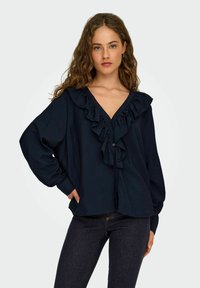 Blouse bleu marine à manches longues avec décolleté en V fringé et fermeture à boutons ; coupe décontractée avec texture douce et léger éclat.