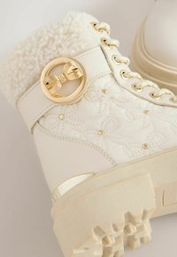 Witte geïsoleerde laars met een faux fur kraag, gouden strikaccent, reliëf bloemmotief, dikke zool en veterontwerp.