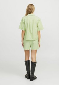 Camicia a maniche corte verde chiaro e pantaloni corti coordinati in un tessuto a strisce texturizzato. Abbinati a stivali neri alti in pelle.