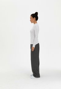 Witte blouse met lange mouwen gecombineerd met grijs gestreepte wijde broek en witte sneakers, gepresenteerd vanuit een zijprofielweergave.