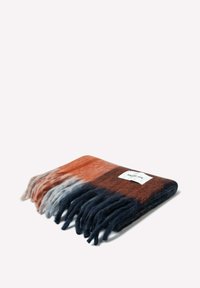Une couverture en laine rectangulaire et multicolore avec des bords frangés. Elle présente des sections orange, grises et marines. Une étiquette blanche est cousue sur un côté.