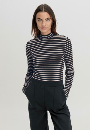 Langarm turtleneck top met marineblauwe en crèmekleurige horizontale strepen; gecombineerd met hoge taille, loose-fitting zwarte broek. Zachte stoftextuur.