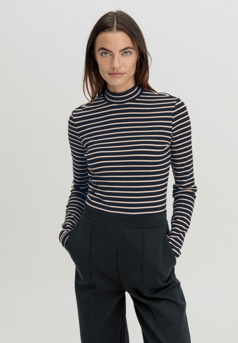 Langärmliges Rollkragenoberteil mit horizontalen Streifen in Marineblau und Creme; kombiniert mit hoch taillierten, locker sitzenden schwarzen Hosen. Weicher Stoff.