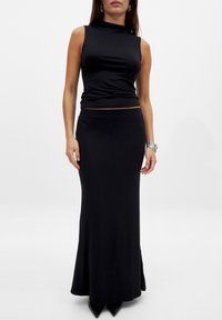 Top nero senza maniche e gonna lunga, aderente, realizzata in tessuto liscio. Il top presenta un collo alto; la gonna ha una silhouette semplice.
