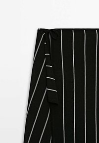 Jupe portefeuille en maille noire avec des rayures blanches verticales et une fermeture à nouer à la taille, présentée sur fond blanc.
