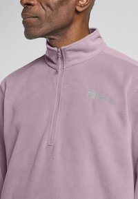 Helllila Fleece-Pullover mit einem Halb-Reißverschluss-Kragen und gesticktem Logo. Weiche Textur, lockere Passform und minimale Nähdetails.