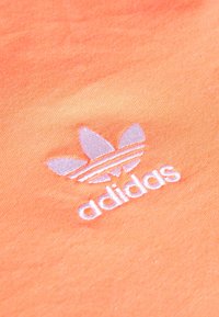 Orange cotton fabric with a subtle texture, featuring a light pink embroidered Adidas logo and three signature stripes above.