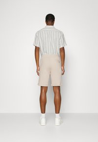Short-sleeved striped shirt in blue and white, paired with beige shorts. Smooth texture, relaxed fit, and casual white sneakers.