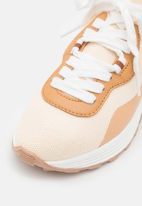 Beige textil a světlé kožené tenisky s bílými šňůrkami, s texturovaným svrškem, polstrovanou podrážkou a kulatou špičkou.