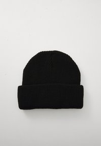 Berretto lavorato a maglia nero con risvolto, posato in piano su una superficie chiara e liscia.